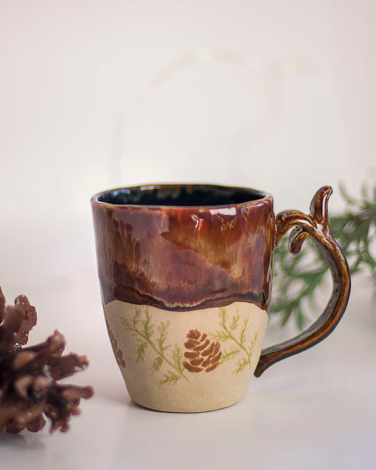 Handbuilt ceramic mug with caramel brown glaze and pinecone drawing